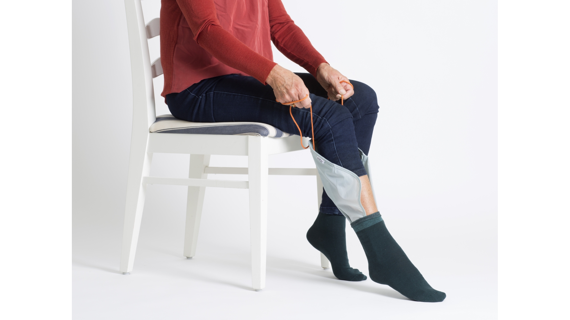 Anziehhilfe aus Gleitmaterial mit festem Mittelstreifen und Bändern, mit dem eine Person eine Socke anzieht, die zuvor drübergezogen wurde