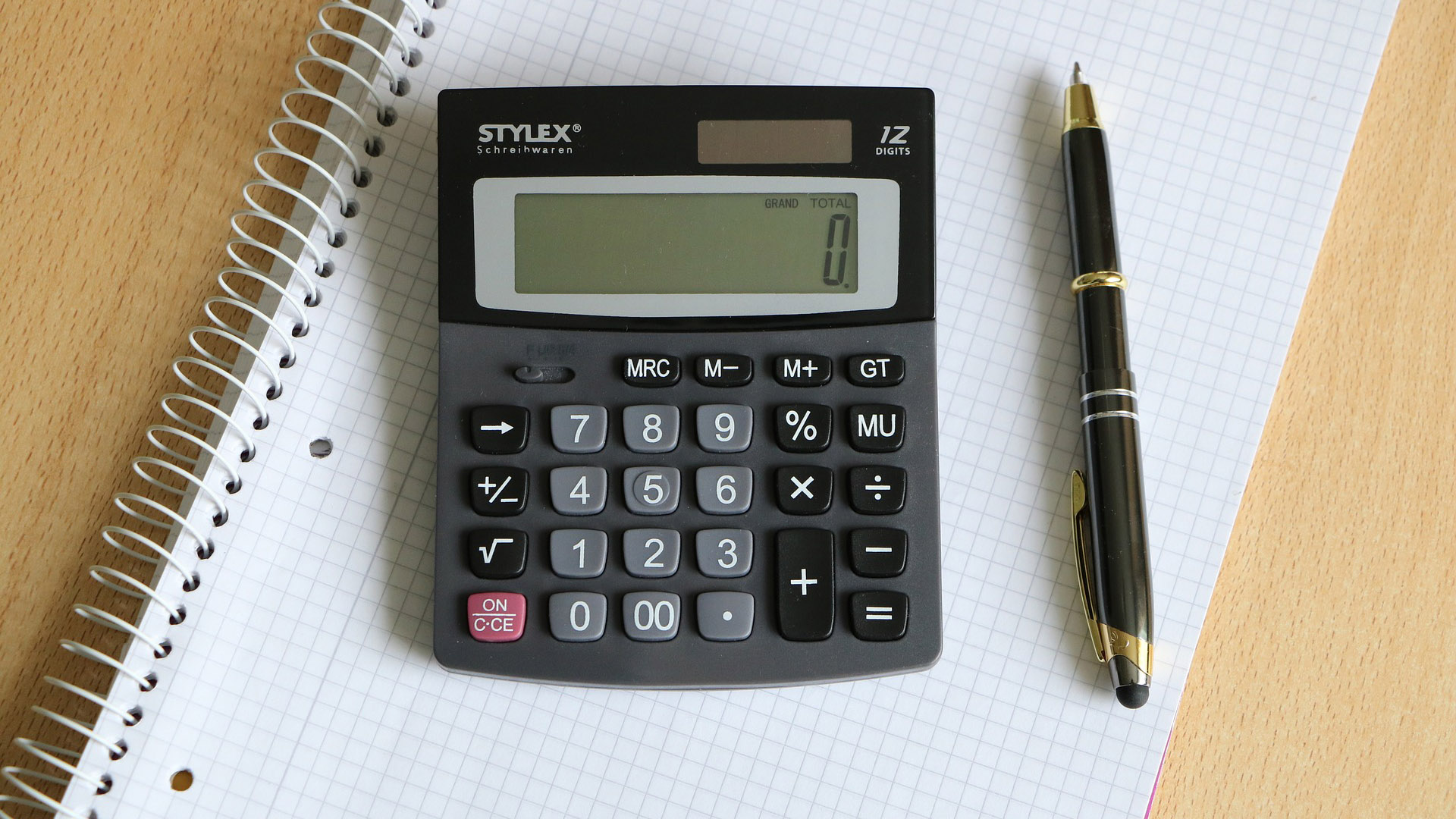 Ein Schreibblock mit Taschenrechner und Stift liegend auf einen Tisch.