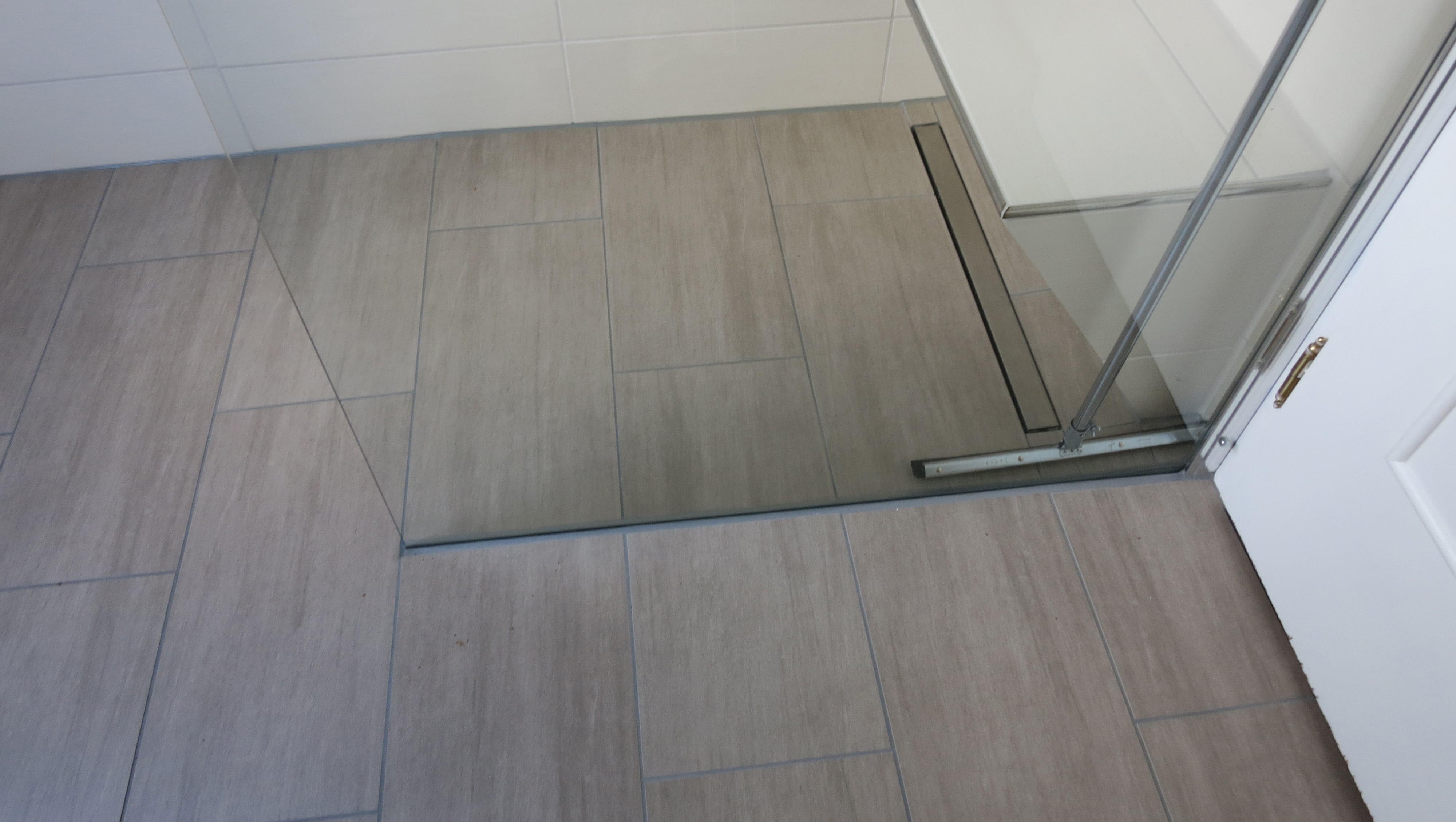 Bodengleicher, gefliester Duschplatz mit einseitiger Glaswand und Ablagebrett.