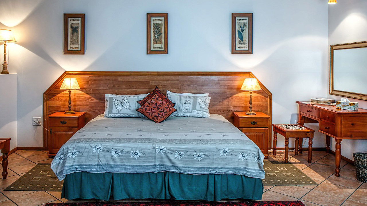 Schlafzimmer mit großem Doppelbett und drei Bildern an der Wand sowie einem Schminktisch mit Spiegel auf der rechten Seite. 