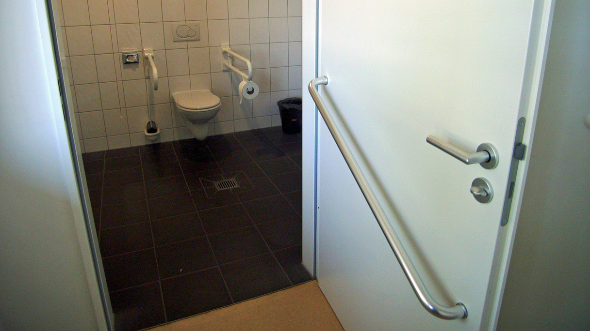 Badezimmertür ohne Schwelle und mit großem Handgriff für Rollstuhlfahrer an der Türinnenseite.