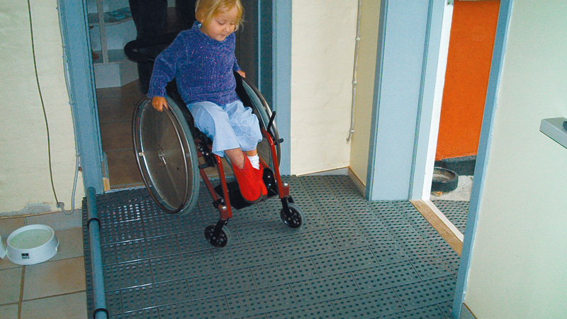 Kind im Kinderrollstuhl auf Türschwellenrampe (Fa. Mohr_Heilmann)