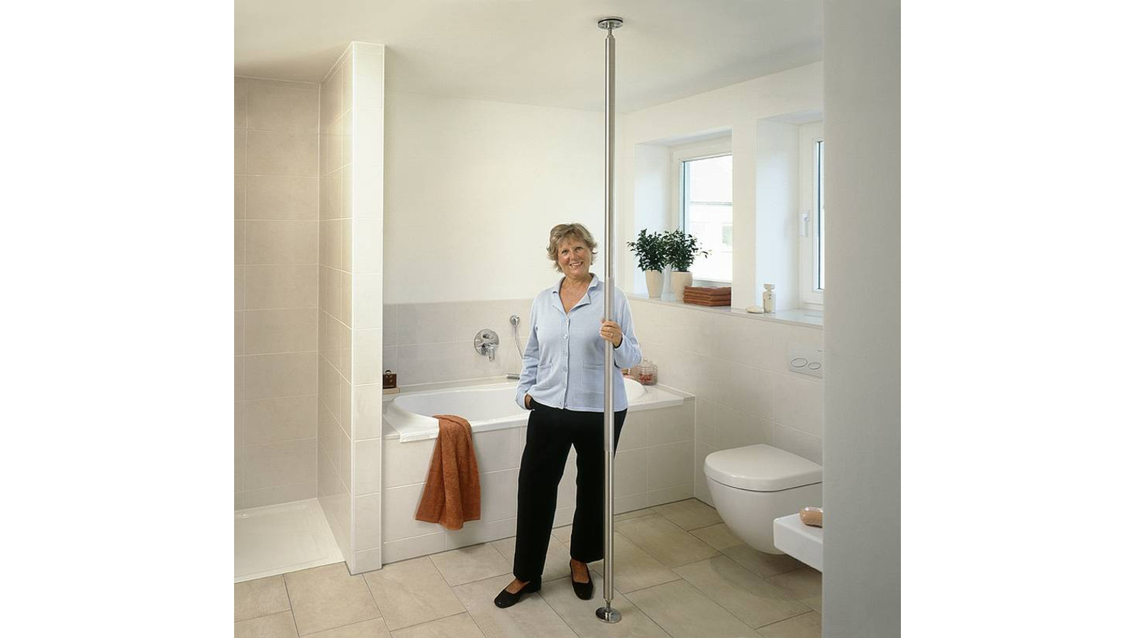 In einem Badezimmer ist eine Klemmstange angebracht vom Boden bis zur Decke, daran hält sich eine Frau fest