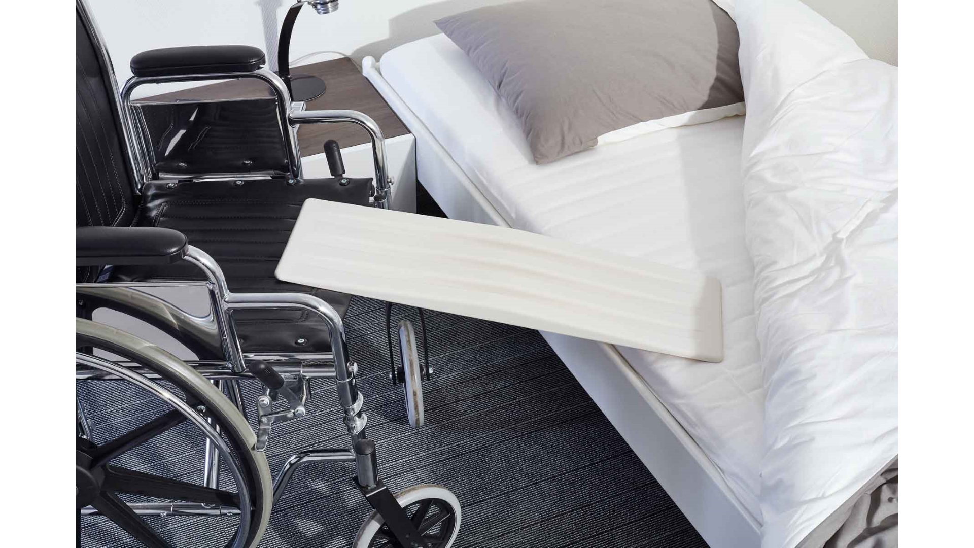 Ein Rutschbrett liegt zwischen Bettkante und Rollstuhl
