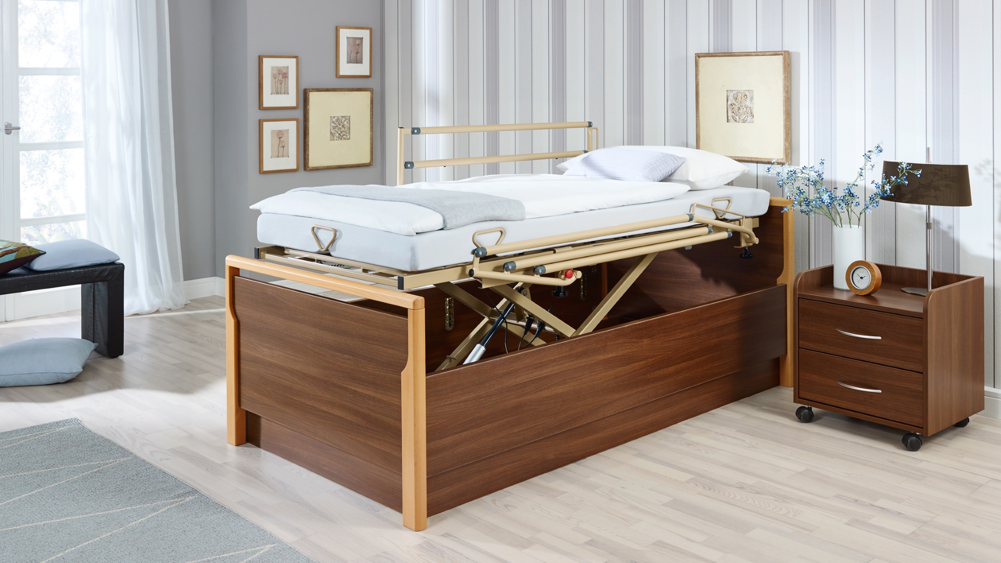 Bett und Nachttisch aus Holz. Ein nach oben gefahrener Betteinsatz zeigt an, dass die Höhe verstellbar ist.
