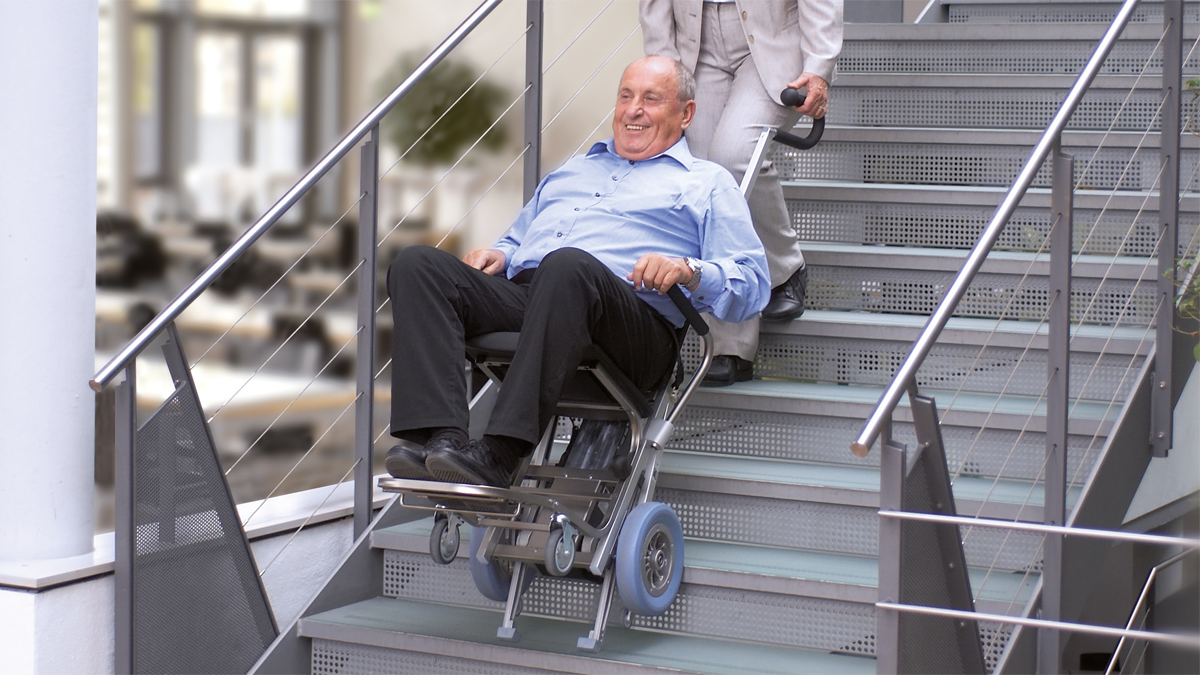 Ein Mann wird sitzend in einem Treppensteiger ein Treppe herunter befördert.