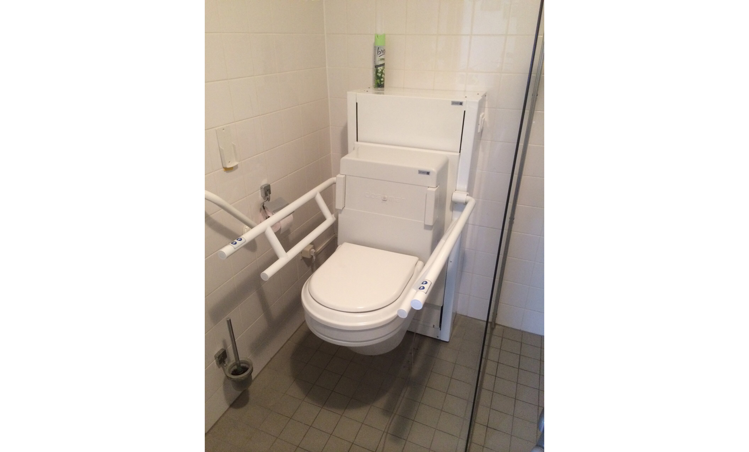Elektrisch höhen- und neigungsverstellbare Lift Toilette mit Stütz-Klapp-Griffen in Aufputzmontage.