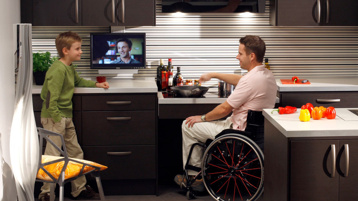 Ein Mann im Rollstuhl bereitet sich an einer unterfahren Arbeitsplatte das Essen zu.
