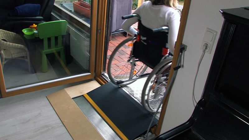 Ein Rollstuhlnutzer fährt über die Türschwellenbühne auf die Terrasse.
