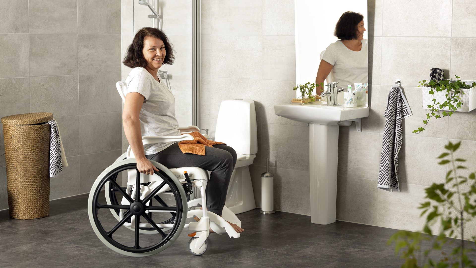 Eine Frau fährt ein WC mit einem Dusch-Toilettenrollstuhl an.
