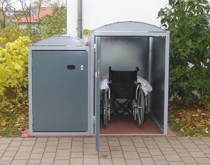 Zwei unterschiedlich große Fertigboxen aus Stahlblech, eine ist geöffnet, in ihr befindet sich ein Rollstuhl.