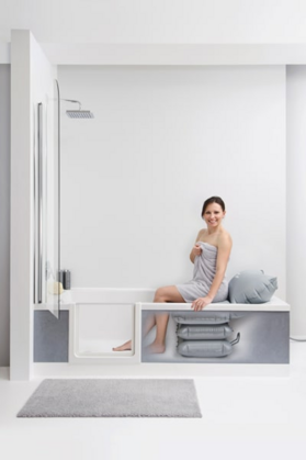 In einer Badewanne mit Tür sitzt eine Person auf einem Badekissen.