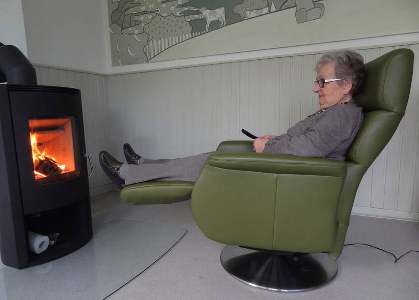 Eine Frau im Relaxsessel vor einem Ofen.