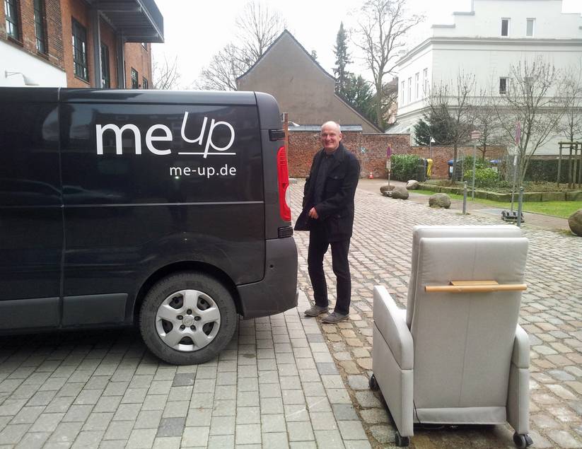 Neben dem Transporter von me-up steht ein Berater mit einem Pflegesessel