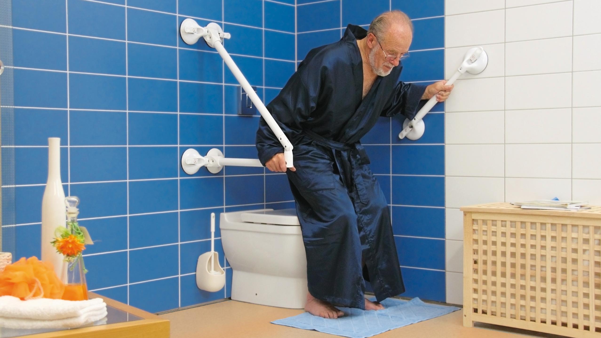 Ein Mann hält sich beim Setzen auf das  WC an mobilen Stütz- und Haltegriffen fest.