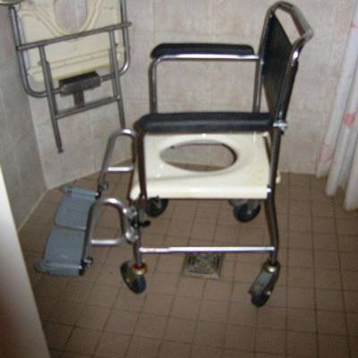 Dusch- und Toilettenschieberollstuhl. Die Sitzfläche hat einen größeren Ausschnitt , der den Gesäß- und Genitalbereich zugänglich hält.