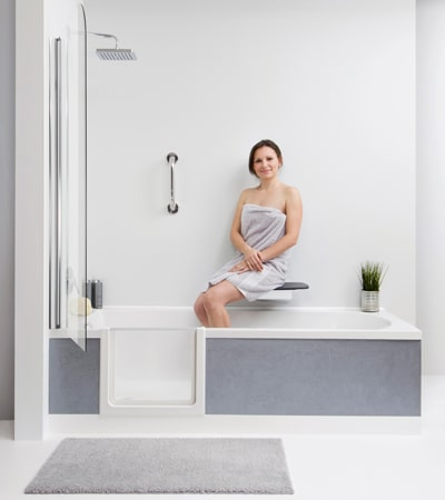 Eine Frau in einer Wanne mit Tür duscht sitzend auf einem Klappsitz.