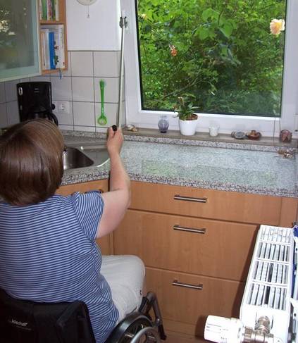 Eine Rollstuhlfahrerin öffnet mithilfe eines manuellen Fensteröffners / einer Fenstergriffverlängerung ein Fenster. (Bild W-Invention)